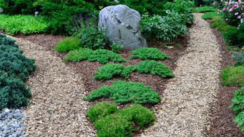 Chitwood Dirt Yard | Rock Hill, SC | two paths made of mulch with green shrubs, rocks, and pink flowers on either side